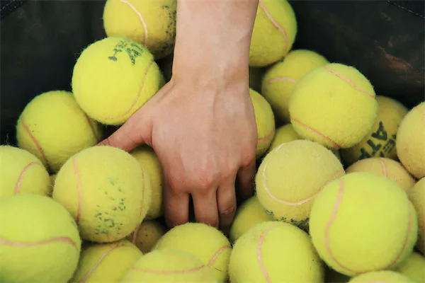 Eine Hand greift in einen Tennisballkorb